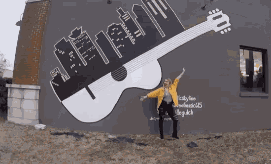 a woman in a yellow jacket stands in front of a large guitar mural