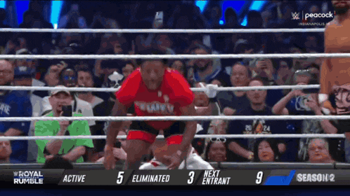 a wrestler in a red shirt is jumping over the ropes during a royal rumble match