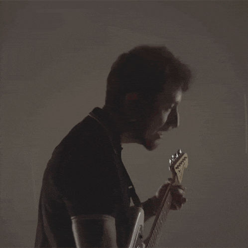 a man in a black shirt is playing a guitar in a dark room