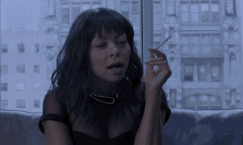 a woman is smoking a cigarette in front of a window .