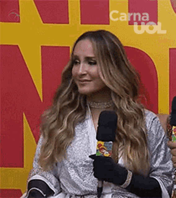 a woman is holding a microphone and smiling while sitting in front of a yellow and red wall .
