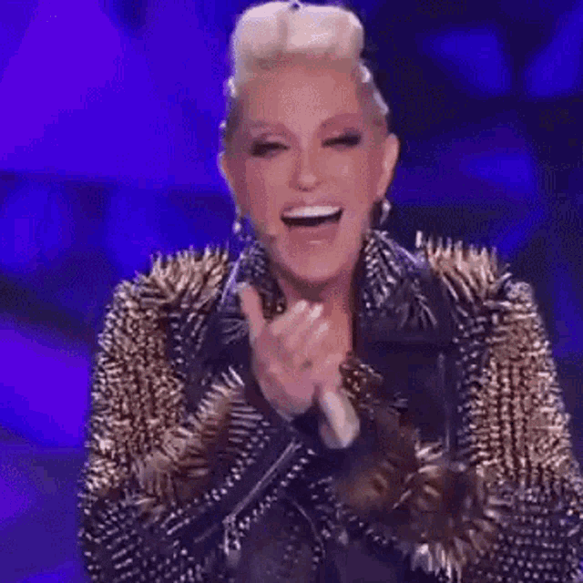 a woman wearing a spiked jacket is laughing and clapping her hands .