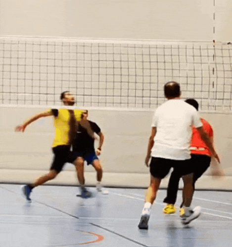 a group of men are playing volleyball and one of them is wearing a yellow shirt