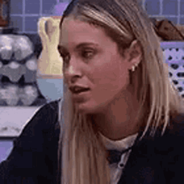 a woman with long blonde hair is sitting at a table in a kitchen with eggs in the background .