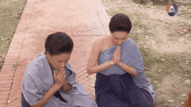 two people praying on a brick walkway with a channel 7 logo visible in the background