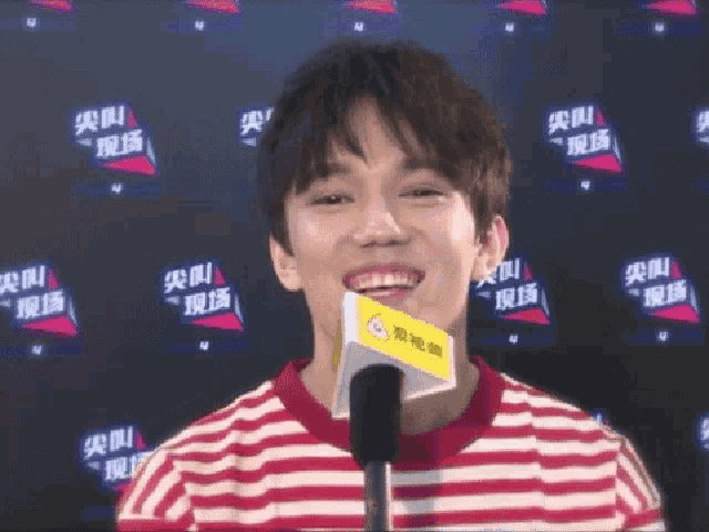 a young man wearing a red and white striped shirt is smiling while holding a microphone