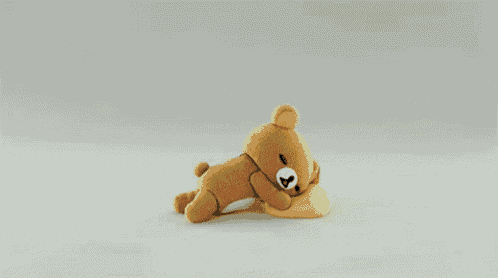 a brown teddy bear is laying on the floor next to a yellow cushion .