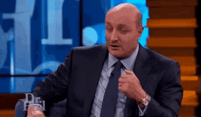 a bald man in a suit and tie is sitting on a stage .
