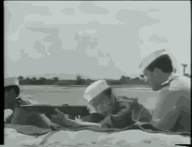 a black and white photo of a group of men laying on a beach .