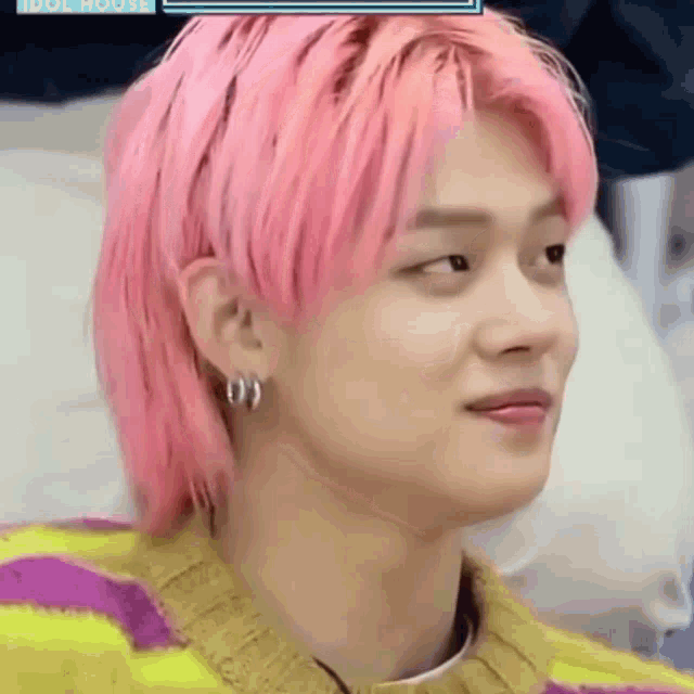 a close up of a person 's face with pink hair and earrings .