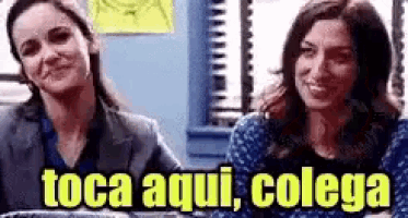two women are sitting next to each other in an office with the words toca aqui , colega written above them .