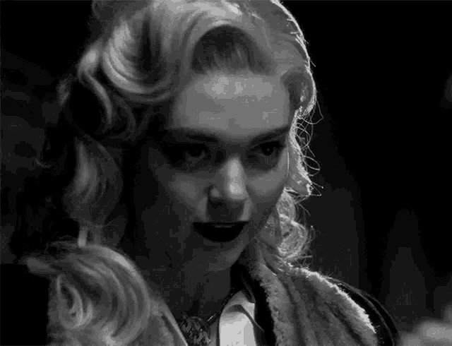 a black and white photo of a woman with blonde hair and black lipstick looking at the camera .