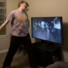 a man in a purple shirt is dancing in front of a large flat screen tv