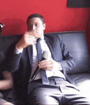a man in a suit and tie sitting on a couch holding a microphone
