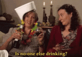 two women are sitting on a couch holding wine glasses and one of them is wearing a toilet paper hat