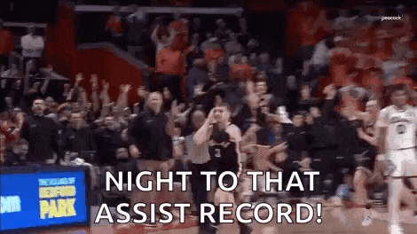 a basketball game is being played in front of a crowd of people and a sign that says `` night to that assist record '' .