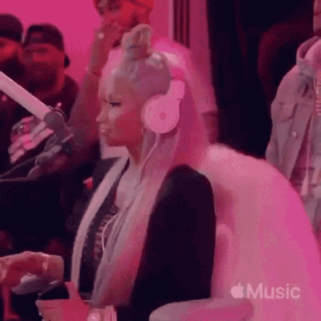 a woman wearing headphones and a fur coat is sitting in front of a microphone in a pink room .