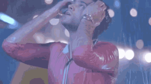 a man in a pink shirt is standing in the rain with his hands on his head .