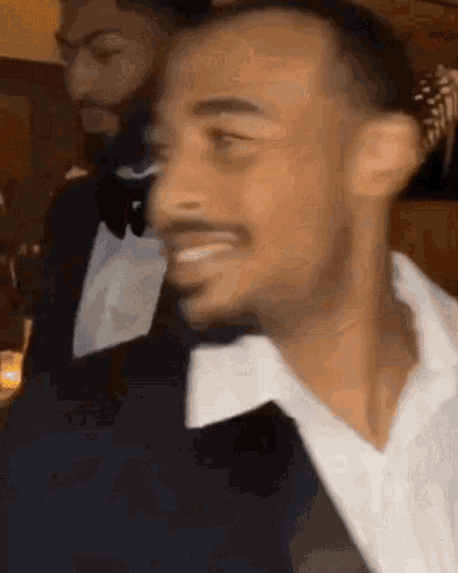 a man in a tuxedo and white shirt is smiling at a party .