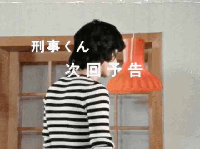 a man in a black and white striped shirt stands in front of a window with chinese writing on it