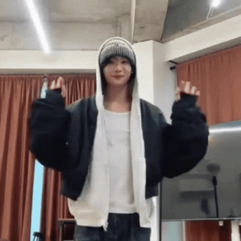 a man wearing a hoodie and a beanie is standing in a room with his arms outstretched .