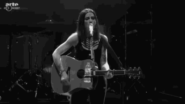 a woman singing into a microphone while holding a guitar in front of an arte concert logo