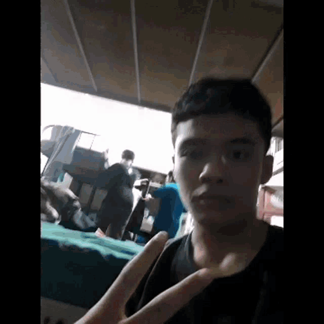 a young man is making a peace sign in front of a group of people in a room .