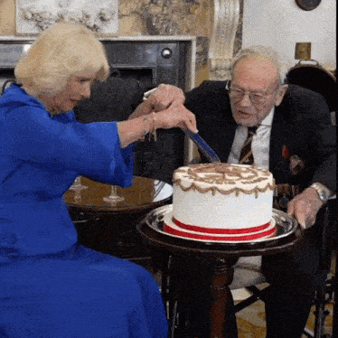 a woman in a blue dress is cutting a cake with an older man