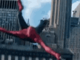 a person in a red spiderman suit is flying through the air in front of a city .