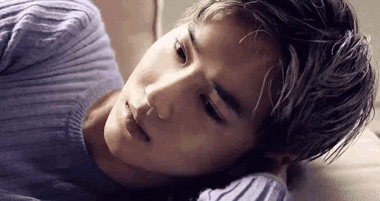 a young man in a purple sweater is laying on a bed with his head on his arm .