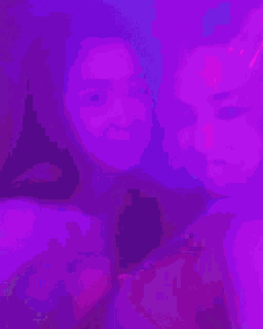 two women are standing next to each other in a dark room with purple lights behind them .