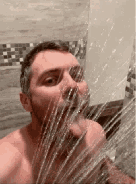 a man is taking a selfie in a shower with water coming out of his face .