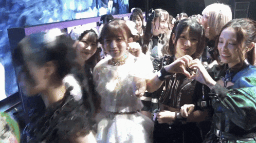 a group of girls are posing for a picture and one girl is making a heart shape with her hands