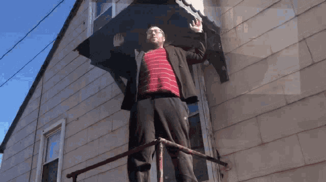 a man in a red striped shirt is standing on a railing in front of a house