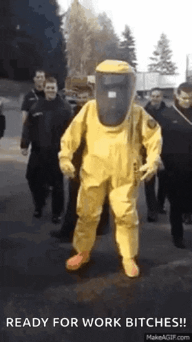 a man in a yellow hazmat suit is walking down a street with a group of people .