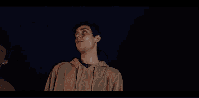 a man in a tan sweatshirt is standing in the dark with his eyes closed