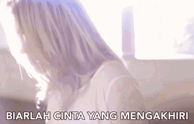 a woman with long blonde hair is sitting in front of a window with the words biarlah cinta yang mengakhiri above her