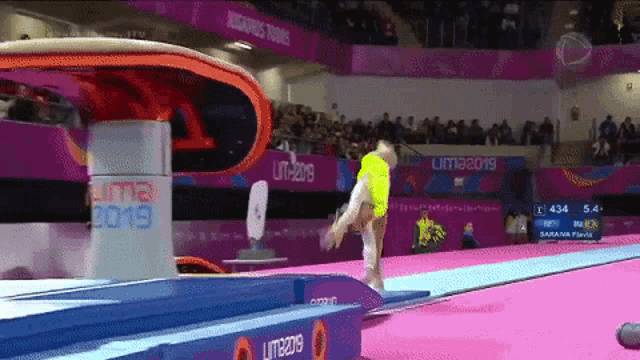 a gymnast is doing a trick on a trampoline in front of a sign that says lima 2019