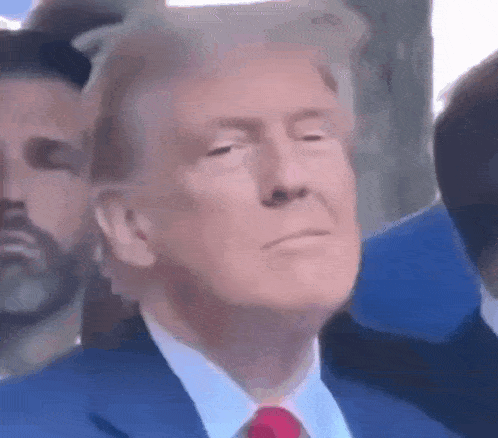 donald trump is wearing a blue suit and red tie while sitting in front of a crowd .