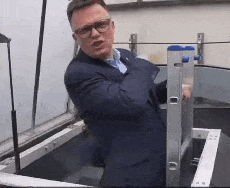 a man in a suit and glasses is standing next to a ladder in a room .