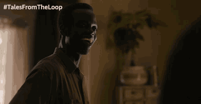 a man in a brown shirt is smiling in a room with #tales from the loop written on the bottom