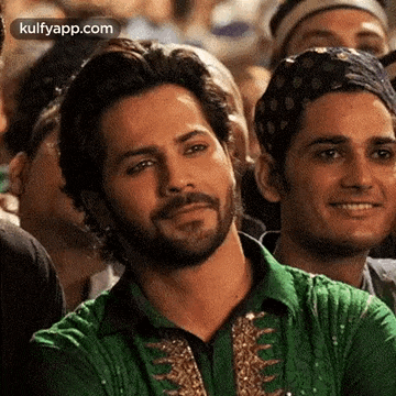a man in a green shirt is sitting in a crowd of people .