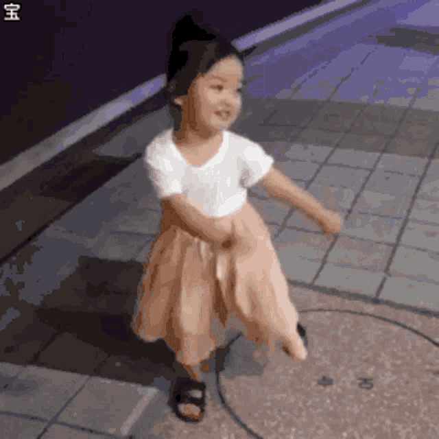 a little girl in a white shirt and a pink skirt is dancing