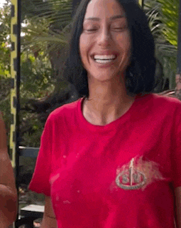 a woman in a red t-shirt is smiling and holding a glass .