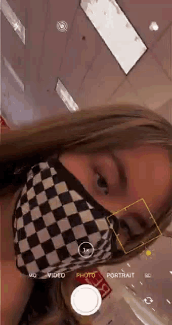 a girl wearing a checkered face mask is taking a picture of herself .