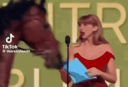 a woman in a red dress is speaking into a microphone while a horse licks her face