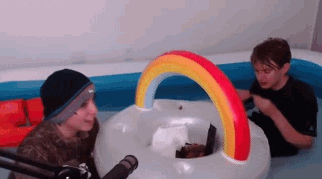 two boys are sitting in a pool with a rainbow inflatable raft .