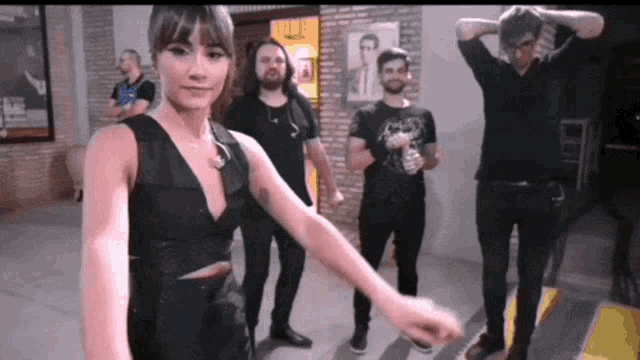 a woman in a black dress stands in front of a group of men in black shirts