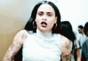 a woman with a lot of tattoos on her arms is wearing a white tank top .