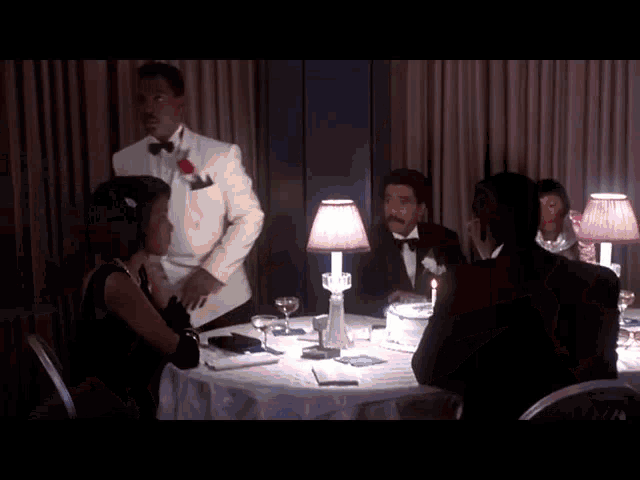 a man in a tuxedo is standing in front of a table with a lamp on it